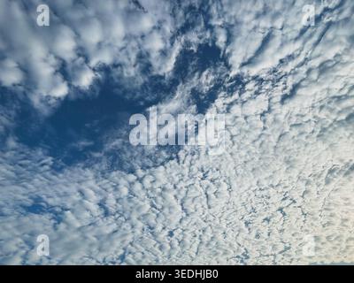 A vibrant blue sky partially covered by a thick layer of textured white clouds, with a clear opening revealing the expanse of the sky. Stock Photo