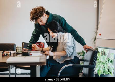 Two students collaborating on paperwork at a table during a tutoring session in a modern classroom Stock Photo