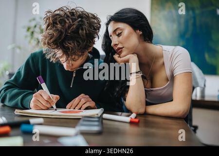 Two students collaborating on a drawing at a table while one guides the other Stock Photo
