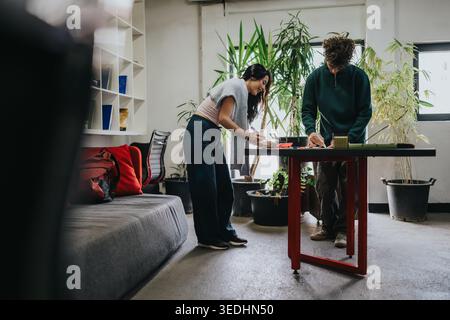 Two students collaborating on a creative project at a casual indoor workspace with potted plants Stock Photo