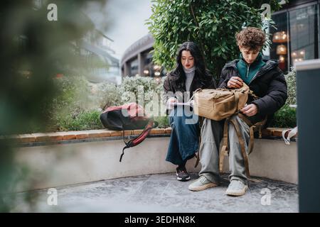 High school friends studying together with backpacks on a city bench outside a cafe Stock Photo