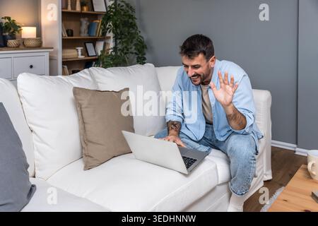 Smiling man working remotely on a laptop during a home office session, enjoying an online conversation, virtual consultation, or casual freelance proj Stock Photo