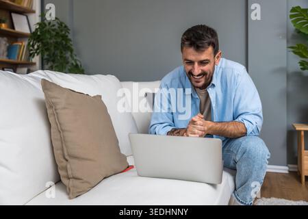 Smiling man working remotely on a laptop during a home office session, enjoying an online conversation, virtual consultation, or casual freelance proj Stock Photo