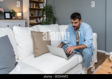 Smiling man working remotely on a laptop during a home office session, enjoying an online conversation, virtual consultation, or casual freelance proj Stock Photo