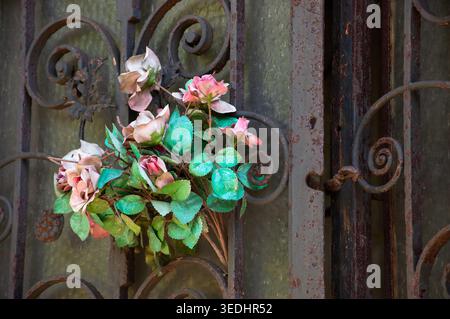 Old cemetery. Faded rose wreath hanging on tomb door. Stock Photo