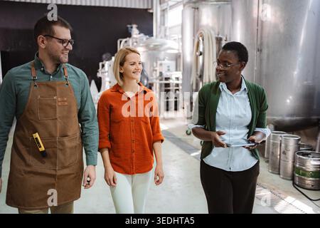 Three diverse colleagues walking through a modern brewery facility and discussing operations Stock Photo