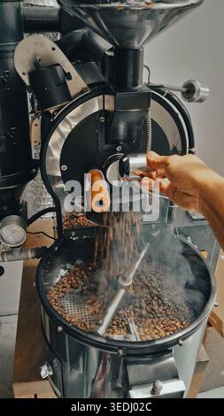 Coffee roasting process using 1 kg capacity manual drum coffee roasting machine, releasing smoking hot roasted coffee into cooling tray by hand Stock Photo
