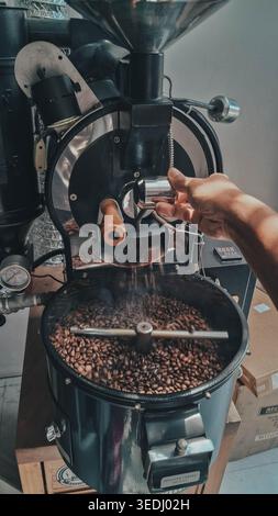 Coffee roasting process using 1 kg capacity manual drum coffee roasting machine, releasing smoking hot roasted coffee into cooling tray by hand Stock Photo