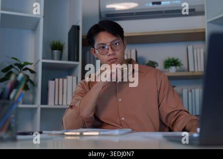 Asian man in 20s working late at home office, focused on laptop Stock Photo