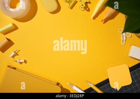 Frame made from stationery items. A notepad, pencils, felt-tip pens, stickers and an eraser against a yellow background. Copyspace Stock Photo