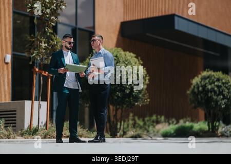 Two businesspeople reviewing documents outdoors in front of a modern office building Stock Photo