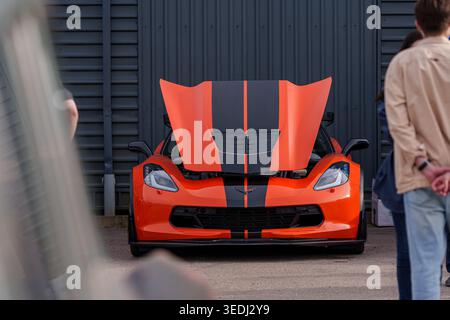 Front view of an orange Chevrolet Corvette C7 Z06 with black racing stripes and open hood, high-performance American sports car on display at an Stock Photo
