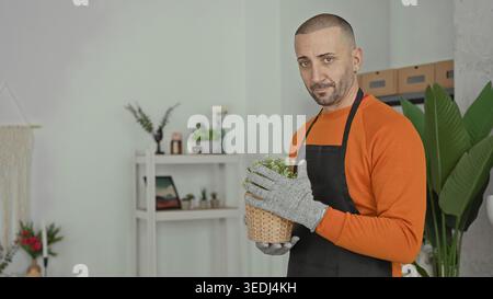 Man florist smelling a potted plant, nose close to tiny white flowers, holding wicker basket in a building; gentle care serenity. Stock Photo