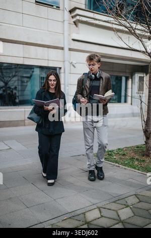 Two students learning outdoors walking and studying together near a campus building Stock Photo
