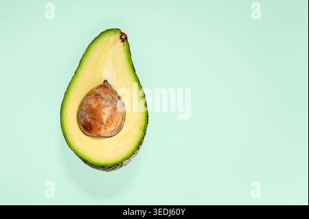 Fresh halved avocado with pit on a mint green background, shot from above with copy space on the right side. Stock Photo