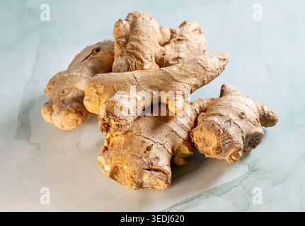 Fresh whole ginger root with textured skin placed on a light marble surface, photographed in close-up with natural lighting. Stock Photo