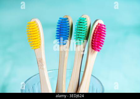 Four eco-friendly bamboo toothbrushes with colorful bristles in yellow, blue, green and pink, arranged in a clear glass against a turquoise background Stock Photo