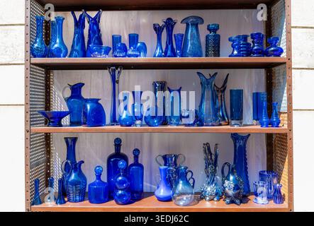 Assortment of decorative blue glass vases, bottles, and bowls on wooden shelves Stock Photo