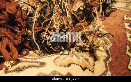 Oriental carpets and tangled wool threads in the market. "From material to product" concept. Selective focus on the threads. Aged photo. Sepia. Stock Photo