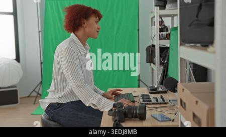 Woman typing on keyboard beside a dslr camera on the table in studio, using monitor and control panel for editing and color grading; creative concentr Stock Photo