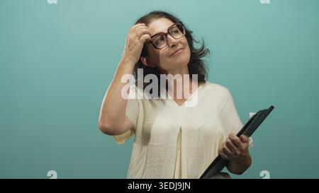Woman holding clipboard and touching hair with glasses, hand to head gesture in studio; serenity confidence ease. Stock Photo