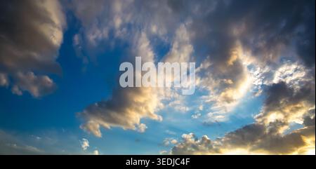 A vibrant blue sky features dynamic gray and white clouds illuminated with yellow, creating a textured appearance across the scene Stock Photo