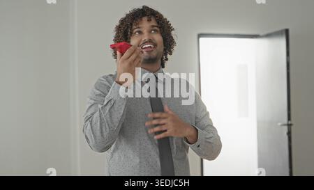 Man in shirt and tie holding red smartphone to mouth, gesturing with hand in building; confident sales pitch. Stock Photo
