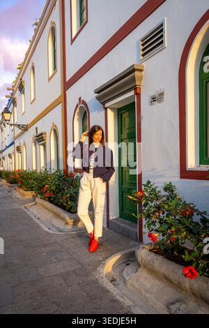 Young Caucasian Curly Haired Woman in Denim Jacket and White Jeans Posing in Puerto de Mogan Street Stock Photo