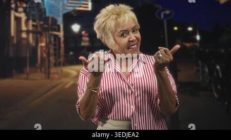 Woman beckons with both hands while smiling on a night street with lampposts and bicycles; welcoming cheerful. Stock Photo