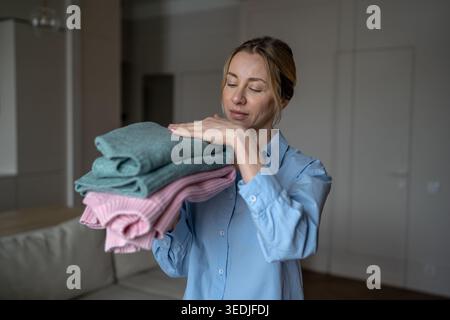 Satisfied woman feeling soft freshly washed sweaters in hands, enjoying tactile pleasure soft fabric Stock Photo