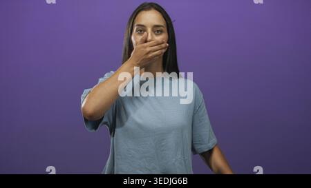 Young hispanic woman covering mouth with hand and pointing thumb to herself in a purple studio; silence secrecy. Stock Photo