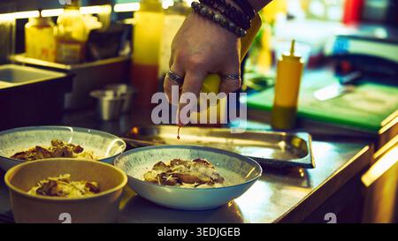 Chef drizzling sauce over creamy chicken pasta bowls in restaurant kitchen. Stock Photo
