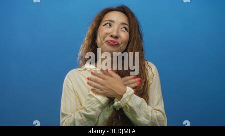 Woman with hands on chest and open mouth expression in blue studio wearing striped shirt and red nail polish; warm gratitude. Stock Photo