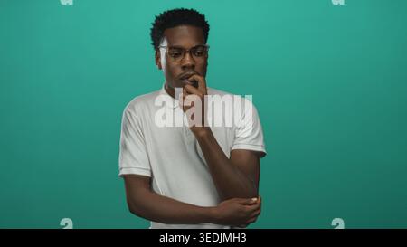 Man with finger on chin gesture in green studio, wearing eyeglasses and white polo shirt; contemplation. Stock Photo