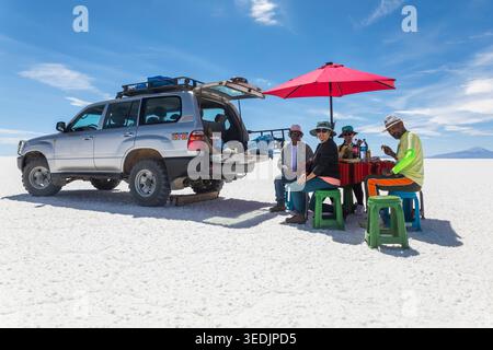 A group of tourists and their guide enjoy an outdoor meal directly on the surface of the Salar de Uyuni, the world's largest salt flat located in Poto Stock Photo