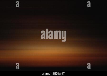 A dark and atmospheric motion blur image capturing the warm glow of a sunset horizon fading into deep shadows. Stock Photo
