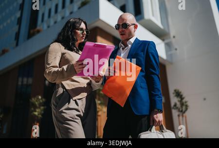 Two business colleagues reviewing colorful document folders outdoors in front of modern office building Stock Photo