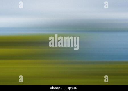An abstract, impressionistic landscape photograph featuring horizontal motion blur, blending vibrant green fields with a soft blue sky and clouds. Stock Photo
