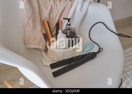 Hair care items like a straightener, brushes, and liquid soap on a white chair Stock Photo