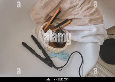 Hair straightener, brushes, and towels on a white surface, representing hair beauty and self-care Stock Photo