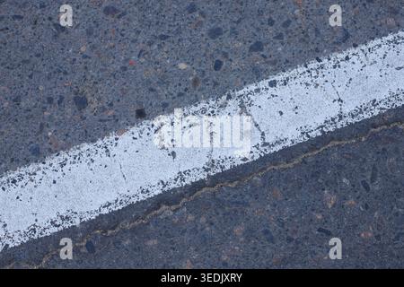 Worn painted line on a stony pavement surface with visible aging and cracks. Urban traffic marking detail showing industrial infrastructure wear. Grit Stock Photo