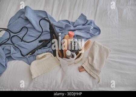 Hair styling tools and natural beauty products spread on a white bed sheet Stock Photo