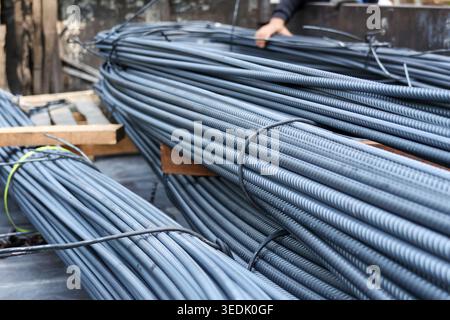 Focused worker handling heavy bundle of steel rebar for construction. Raw iron metal material secured with wire on truck ready for industrial building Stock Photo
