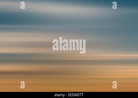 A textured abstract background with soft horizontal streaks of blue, gray, and orange, reminiscent of a sunset or twilight sky. Stock Photo