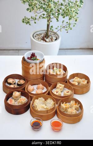 assorted dimsum on traditional bamboo steamer basket on top of white table with white background Stock Photo