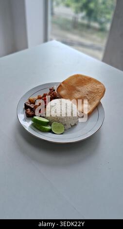 an indonesian traditional food from central java, oseng mercon, diced beef braised in herbs and chili, with rice, sliced cucumber and fish crackers Stock Photo