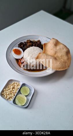 an indonesian traditional food from east java, a black coloured beef stew served with rice, called rawon, served in a white plate on white table Stock Photo