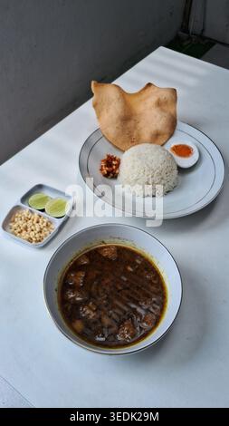 an indonesian traditional food from east java, a black coloured beef stew served with rice, called rawon, served in a white plate on white table Stock Photo
