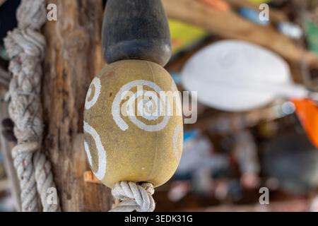 Close view of rustic wooden buoy with white spiral pattern hanging on thick rope. Traditional nautical decoration evoking peaceful feeling by sea in b Stock Photo