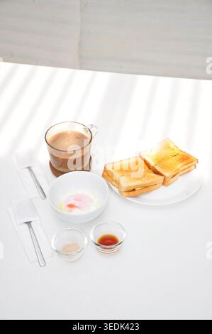 a typical kopitiam style breakfast set consist of kopi susu or sweet milk coffee, kaya toast and soft boiled egg, served in a white table Stock Photo